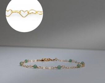 May include: A delicate gold chain bracelet featuring a series of interconnected heart-shaped links and small, round, light green beads spaced evenly along the length of the chain, with a circular inset showing a close-up of the heart link design.
