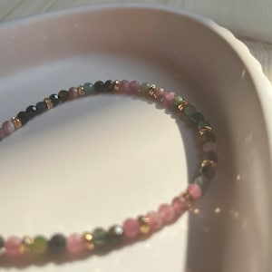Puede incluir: Un brazalete delicado hecho con peque&ntilde;as cuentas redondas en tonos rosa, verde y negro. Las cuentas est&aacute;n intercaladas con peque&ntilde;as cuentas doradas.