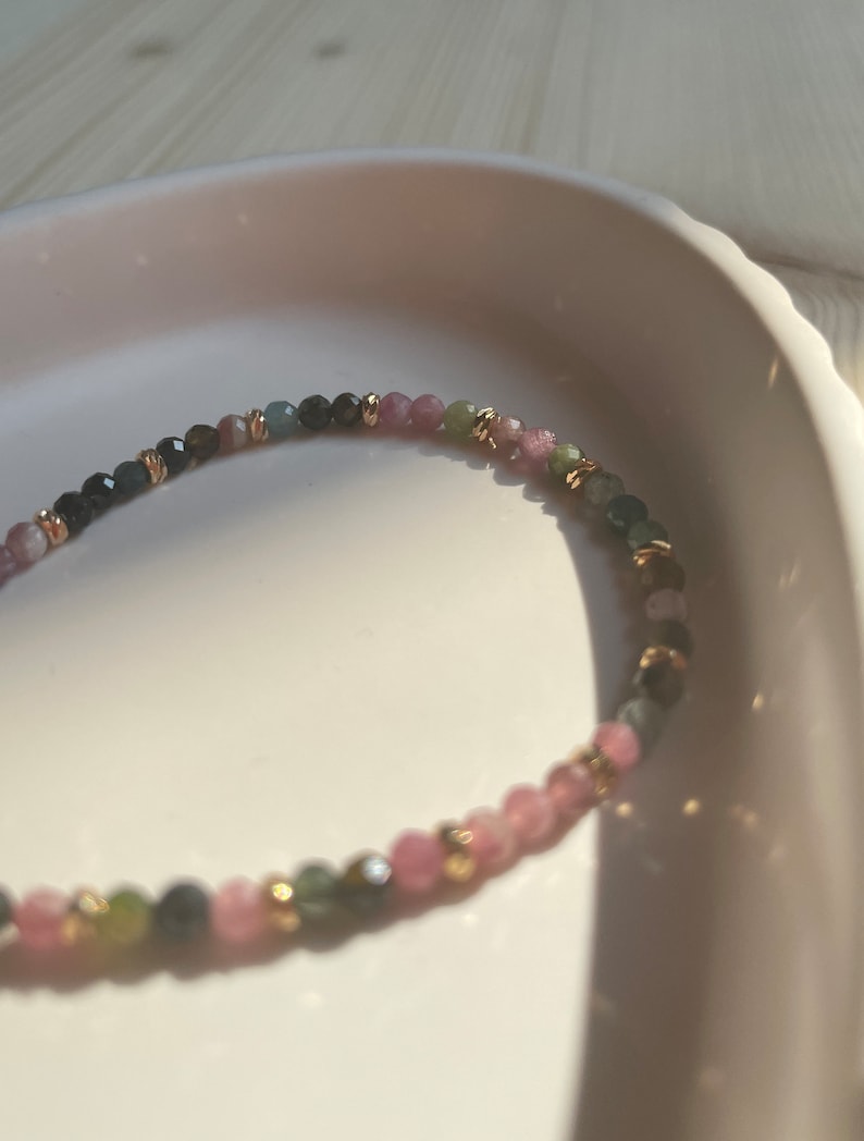 Puede incluir: Un brazalete delicado hecho con peque&ntilde;as cuentas redondas en tonos rosa, verde y negro. Las cuentas est&aacute;n intercaladas con peque&ntilde;as cuentas doradas.