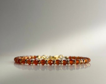 May include: A delicate gold bracelet with small, round, orange carnelian beads.