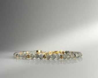 May include: A delicate bracelet made with light gray gemstone beads and gold accents.