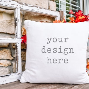 May include: White pillow with the text "your design here" on a rustic wooden bench with a weathered window frame and fall leaves.