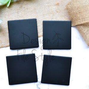 May include: Four black square coasters with a simple branch design on one of the coasters. The coasters are on a white marble surface with a piece of burlap fabric in the background.