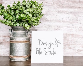 May include: A white card with the text "Design File Style" in gray script font with a small gray twig design next to the word "Design". The card is sitting on a wooden surface next to a galvanized metal pitcher with a green leafy plant.