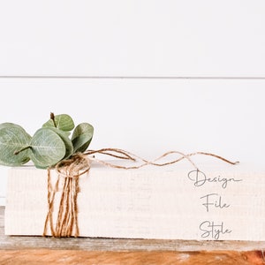 May include: A white wooden block with the words "Design File Style" written on it. The block is wrapped in twine and decorated with a sprig of eucalyptus.
