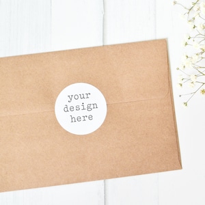 May include: A brown paper envelope with a white circle sticker that says "your design here" on a white wooden surface.