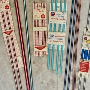 May include: A collection of vintage knitting needles and crochet hooks in various colors including red, blue, and silver. The set includes packaged Ezy-Knit aluminum needles, Boye plastic double point needles, and loose metal crochet hooks.