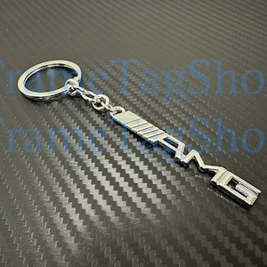 May include: Silver metal keychain with a silver AMG logo. The keychain has a silver ring for attaching keys.