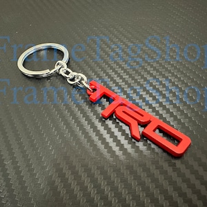 May include: Red metal keychain with the word "TRD" in raised letters. The keychain is attached to a silver metal ring.
