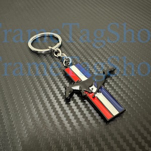 May include: A silver key chain with a black and red metal charm featuring a stylized horse and stripes.