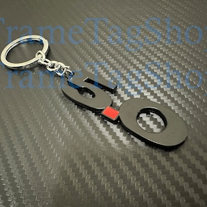 May include: Black metal keychain with the number 50 in a bold font. The number 0 has a red accent. The keychain is attached to a silver key ring.