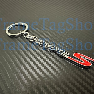 May include: Silver keychain with a black and red "Type R" logo. The keychain has a silver ring and a silver chain.