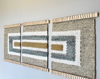 May include: Three woven wall hangings with geometric patterns in shades of brown, beige, white, and gray. The hangings are framed with natural wood.