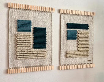 May include: Two woven wall hangings with geometric designs. Each piece features a light beige background with textured teal and dark green squares and beige horizontal lines. The hangings are framed with wooden dowels.