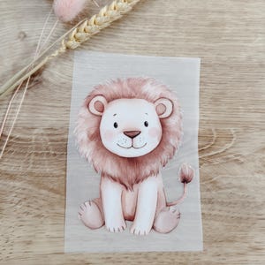 Könnte beinhalten: Aquarell-Illustration eines sitzenden Löwenjungen mit hellrosa Mähne, Ohren und Schwanz. Der Löwe hat ein weißes Gesicht, rosa Wangen und einen kleinen, lächelnden Mund. Das Bild befindet sich auf einem hellgrauen Hintergrund.
