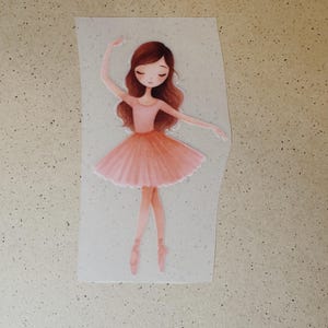 Könnte beinhalten: Aquarell-Illustration einer Ballerina in rosa Kleid und Ballettschuhen. Die Ballerina hat braunes Haar und posiert mit einem erhobenen Arm. Das Bild befindet sich auf einem hellgrauen Hintergrund.