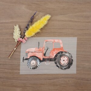 Könnte beinhalten: Aquarellillustration eines roten Traktors mit schwarzen Reifen. Der Traktor befindet sich auf transparentem Hintergrund. Getrocknete Blumen in Gelb, Lila und Weiß sind links vom Traktor angeordnet.