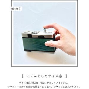 May include: A small, silver and green camera with a button being pressed. The camera has a wooden-like green finish and a silver top. The text in the image describes the camera's size and button feel.