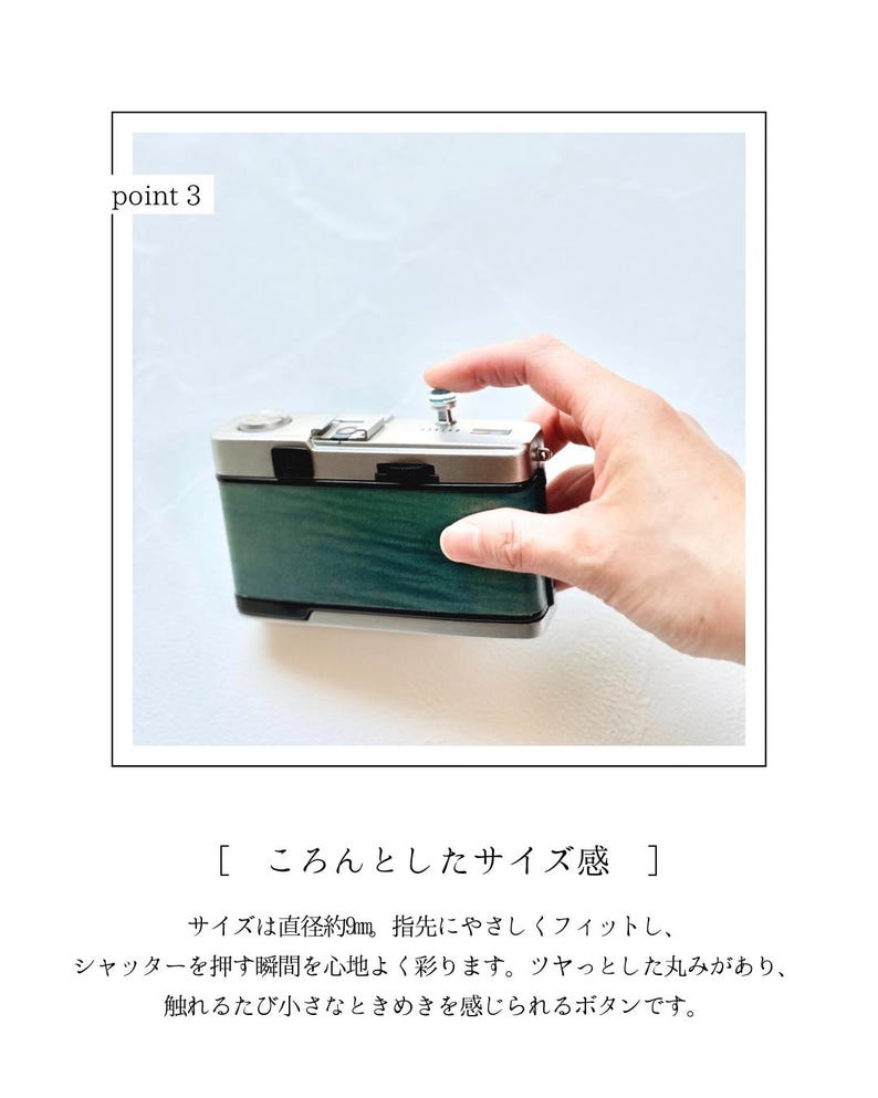 May include: A small, silver and green camera with a button being pressed. The camera has a wooden-like green finish and a silver top. The text in the image describes the camera's size and button feel.