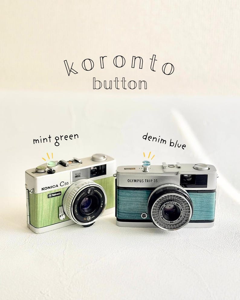 May include: Two vintage cameras, a Konica C35 in mint green and an Olympus Trip 35 in denim blue. Each camera has a coloured button on top. The text "koronto button" is above the cameras.