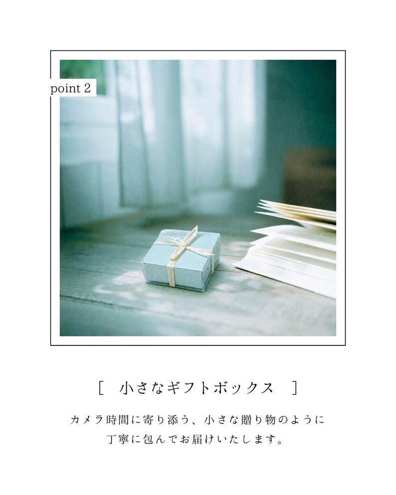 May include: A small, pale blue gift box with a cream ribbon on a wooden surface. An open book with white pages is next to the box. The text "point 2" is in the upper left corner. The box is a charming present.