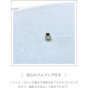 May include: A small, silver button with a green centre, set against a light blue textured background. The text "point 1" is in the upper left corner. The button is likely a camera accessory.