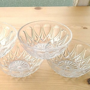 May include: Four clear glass bowls with a diamond pattern on a wooden surface.