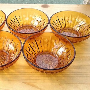 May include: Set of six amber glass bowls with a textured, raised design. The bowls are arranged in a semi-circle on a wooden surface.