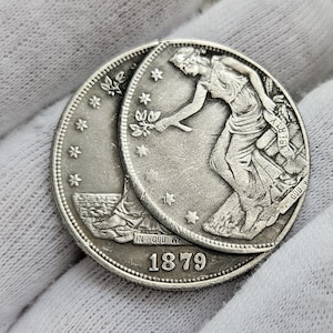 Puede incluir: Una moneda de medio dólar estadounidense de plata de 1879, con la cabeza de la Libertad. La moneda presenta el perfil de la Libertad con el pelo suelto y una corona en la cabeza. La inscripción "LIBERTY" es visible en el lado derecho de la moneda. La moneda está en buen estado con algo de desgaste.