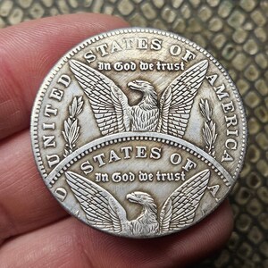 May include: A silver United States coin with an eagle design and the inscription "STATES OF AMERICA" and "In God We Trust".