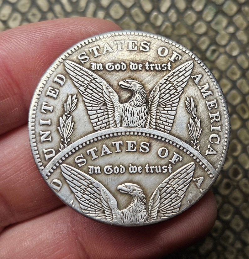 May include: A silver United States coin with an eagle design and the inscription "STATES OF AMERICA" and "In God We Trust".