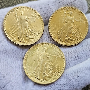 Może przedstawiać: Trzy złote monety amerykańskie o nominale 20 dolarów w kolorze złotym z wizerunkiem Lady Liberty na awersie. Monety są datowane na 1930, 1932 i 1927.