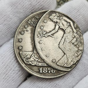 May include: A silver US Morgan dollar coin from 1876. The coin features a profile of Liberty on one side and an eagle on the other.