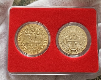 May include: Two gold-colored coins encased in a clear plastic holder with a bright red velvet-like insert. The left coin features two crowned profiles facing each other, while the right coin displays a central cross design with ornate lettering.