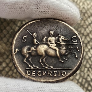 Puede incluir: Una moneda romana de plata con la inscripción "DE CVRSIO" y la representación de dos jinetes a caballo.
