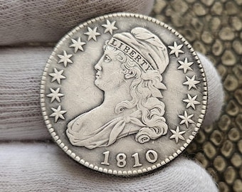 Może przedstawiać: Srebrna moneta dolara z wygrawerowanym rokiem 1810 na dole. Na monecie znajduje się portret Wolności z napisem "LIBERTY" nad głową. Moneta jest otoczona 13 gwiazdami.