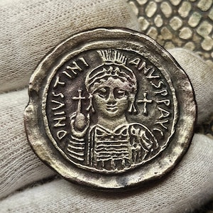 Puede incluir: Una moneda de plata con el retrato de una mujer que lleva una corona y sostiene una cruz. La inscripción alrededor del retrato dice "DNVS IVSTINI AVS SPAV", que es latín para "Dominus Justinianus Augustus Spav" (Señor Justiniano Augusto Spav).