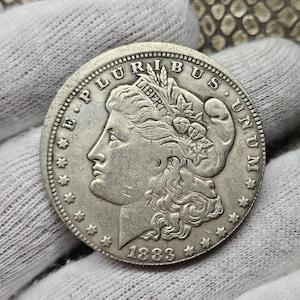 Puede incluir: Una moneda de plata estadounidense Morgan dólar con el año 1883 inscrito en la parte inferior. La moneda presenta un retrato de Lady Liberty con la inscripción "E PLURIBUS UNUM" alrededor del borde.
