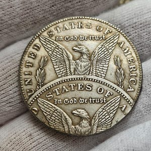 May include: A silver United States of America coin with an eagle design and the words "In God We Trust" on both sides.