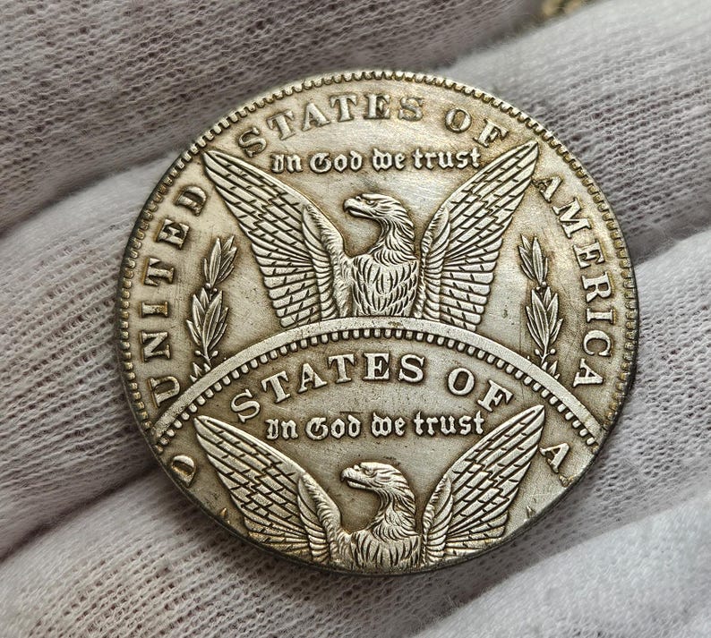 May include: A silver United States of America coin with an eagle design and the words "In God We Trust" on both sides.