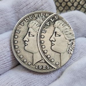 May include: A silver coin split in half, featuring a profile of a woman with the word "LIBERTY" and the year "1921". The coin has the words "E PLURIBUS UNUM" and stars around the edge.