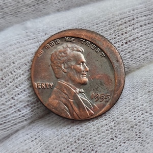 Può includere: Una moneta da un centesimo di dollaro americano in rame del 1955 con il profilo di Abraham Lincoln sul dritto e le parole "In God We Trust" e "Liberty" sulla moneta.