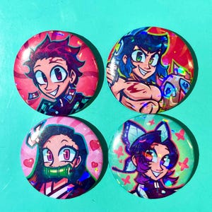 May include: Four circular buttons with anime-style character illustrations. Each button showcases a unique character design in vibrant colours, including pink, blue, and green. The buttons have a glossy, holographic finish.