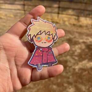 May include: A sparkly, cartoon-style sticker of a character with blonde hair, wearing red clothing and sunglasses. The character is smiling and has a red and white striped shirt.