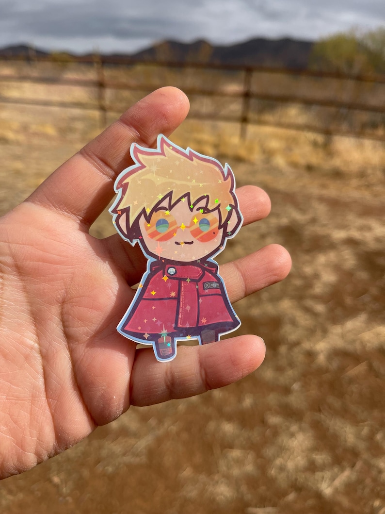 May include: A sparkly, cartoon-style sticker of a character with blonde hair, wearing red clothing and sunglasses. The character is smiling and has a red and white striped shirt.