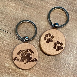Peut inclure: Deux porte-clés en bois avec des anneaux argentés. L'un présente un motif de carlin, l'autre deux empreintes de pattes. Les porte-clés sont en bois clair, adaptés aux amoureux des animaux.