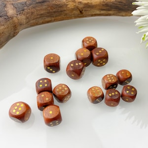 Op de afbeelding: Een verzameling houten dobbelstenen met goudkleurige stippen. De dobbelstenen zijn diep bruin van kleur en liggen verspreid over een wit oppervlak. Klassieke spelaccessoires.