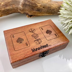 May include: A wooden box with a dark finish, featuring engraved playing card aces and dice. The box has a metal clasp and the text "Wunschtext..." is visible. The overall theme is games and entertainment.