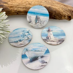May include: Four round wooden coasters with beach scenes. One shows beach chairs and a towel, another a lighthouse, and a third a boat and seagull. The fourth coaster depicts starfish and waves. The coasters are light blue, white, and brown.