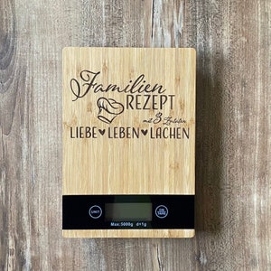 Op de afbeelding: Een bamboe keukenweegschaal met een digitale display. De tekst "Familien Rezept" en "LIEBE LEBEN LACHEN" is gegraveerd. De weegschaal meet tot 5000g met een precisie van 1g.